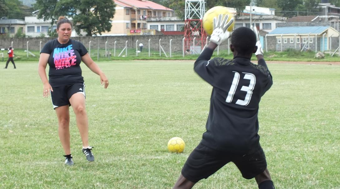 A Projects Abroad volunteer teaching sports in Kenya helps a player practise defending the goal A football player practises defending the goal during volunteer sports coaching in Kenya